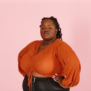 Young confident black plus size body positive woman looks at camera holding hands on waist on light pink background in studio closeup